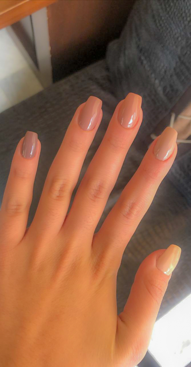 Hand with manicured nails in a gradient of nude and brown shades, resting on textured fabric and wood