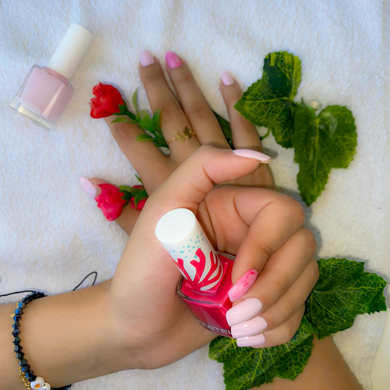 Nails painted in a soft pink shade, accented with a bright pink polish bottle and surrounded by red floral elements
