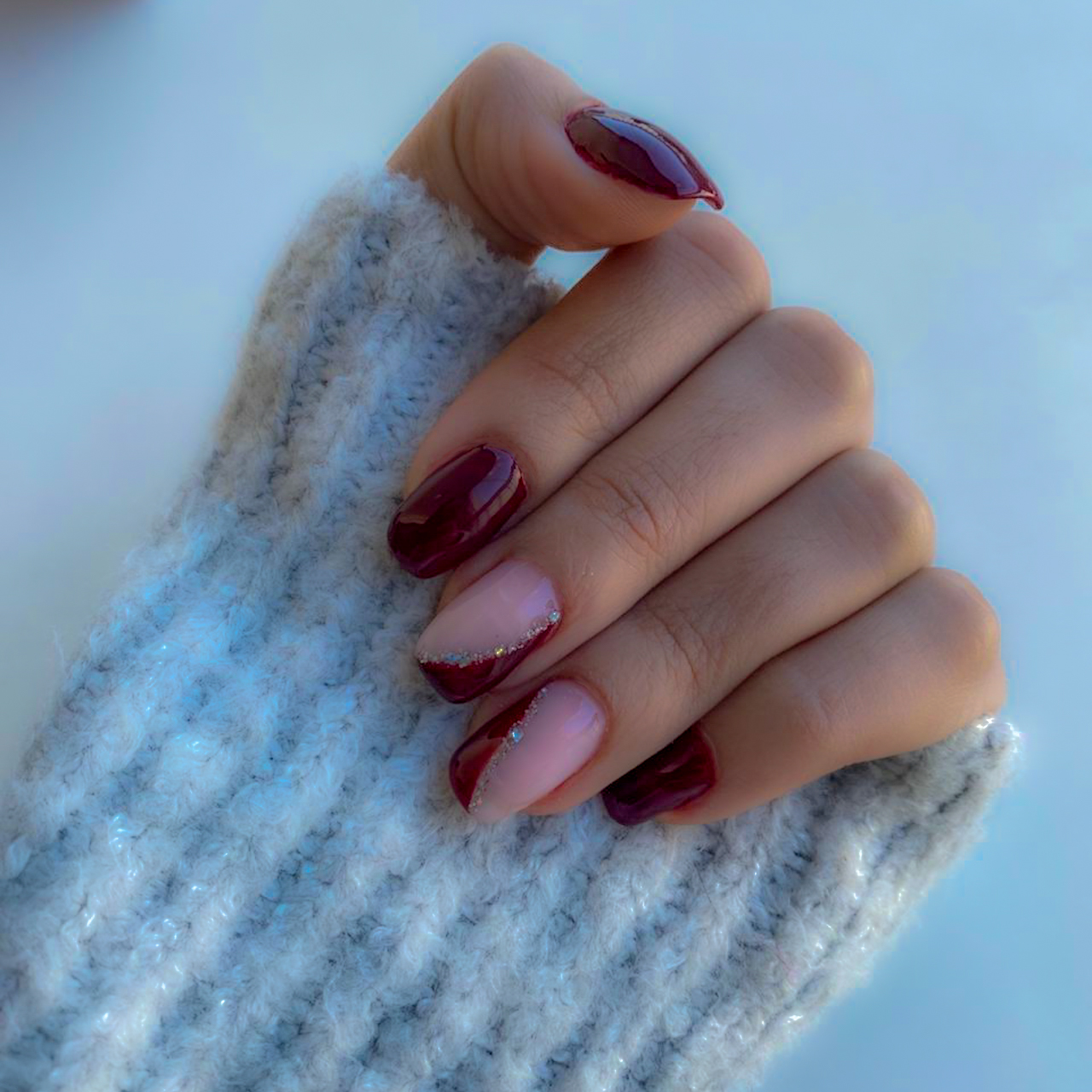 Nails featuring dark red polish alongside soft pink bases with diagonal red tips and silver glitter accents