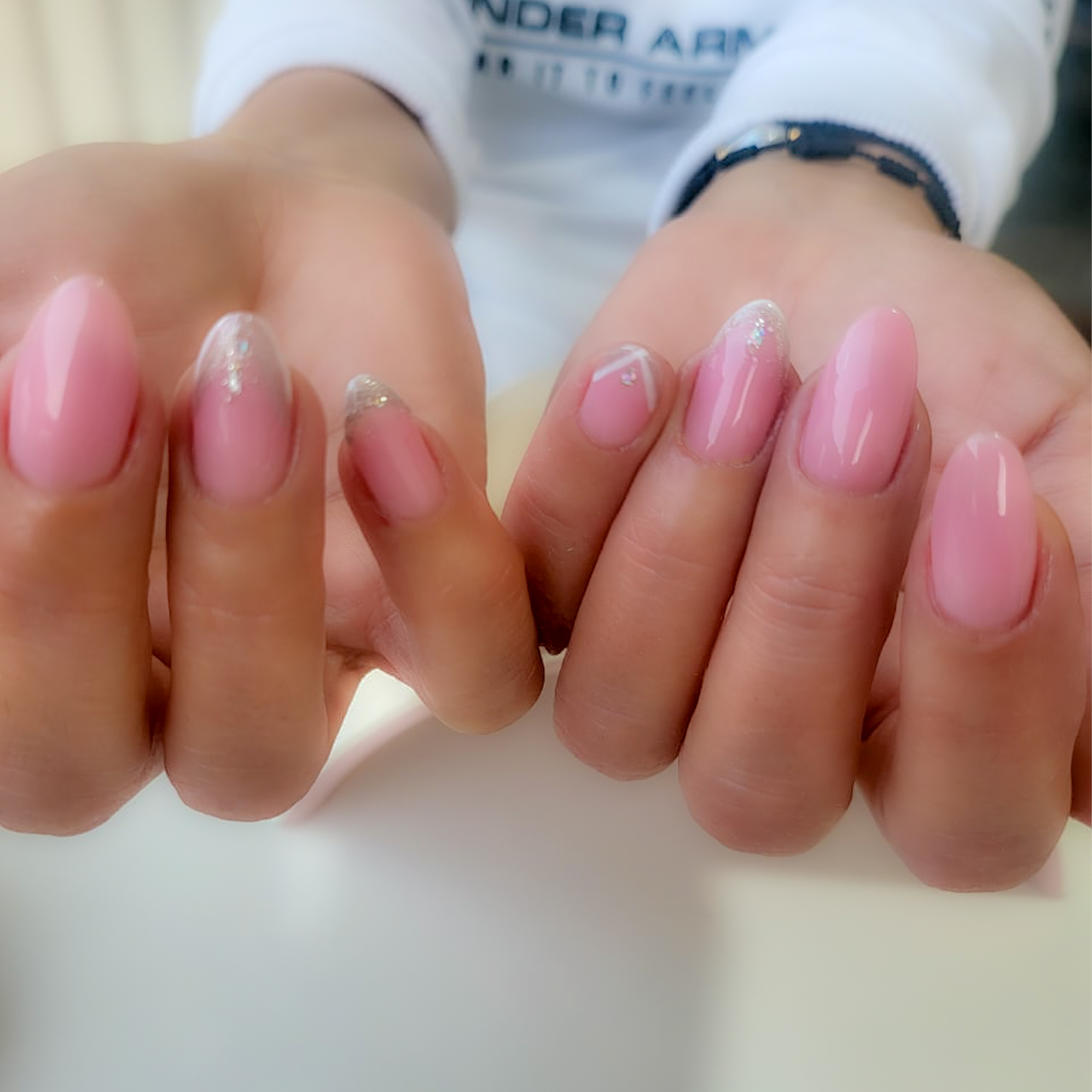 Nails painted in pale pink with a glossy finish, featuring subtle glitter accents near the tips